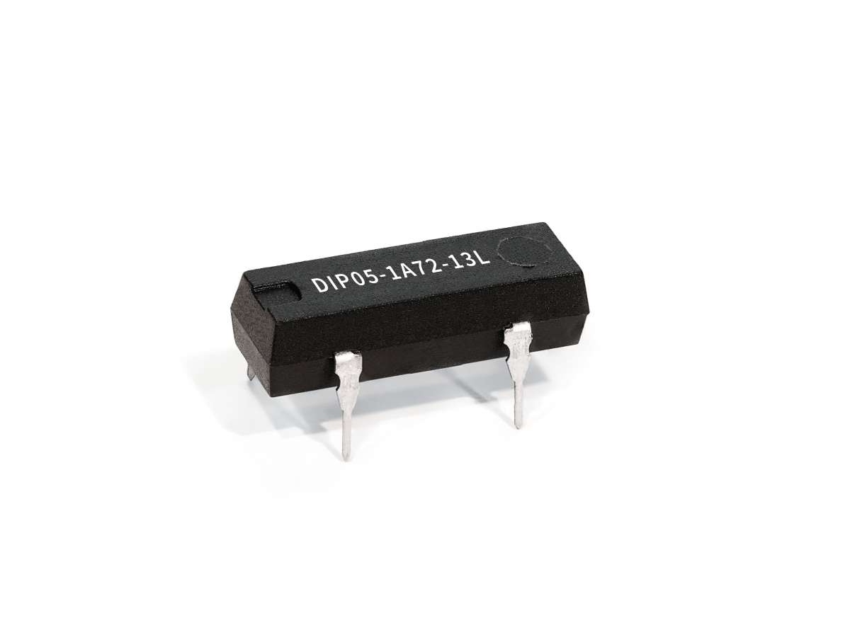 A black integrated circuit chip from the DIP Series Reed Relay family, labeled DIP05-1A72-13L, features four metal pins and is placed on a white background. by Standex Detect