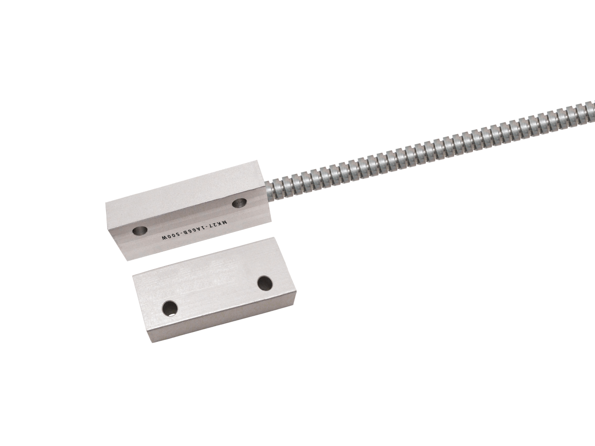 Two rectangular MK27 Series reed sensor components, one connected to a flexible, ribbed cable, are positioned on a white background. Both feature two round holes and engraved text markings. by Standex Detect